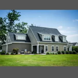 Large two-story house with newly installed gray siding, featuring dormers and a well-maintained lawn.