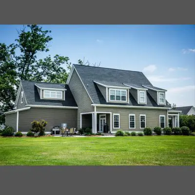 Large two-story house with newly installed gray siding, featuring dormers and a well-maintained lawn.