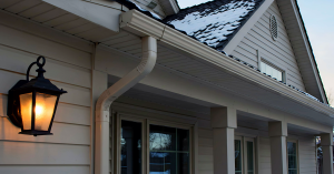 A house with snow on the roof and featured siding with an outdoor lantern on the front.