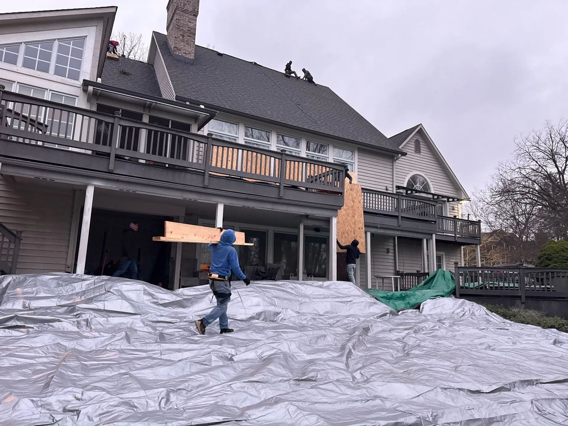Moss Roofing roofers installing a home with a new roof, tarp covering the outdoor area for protection