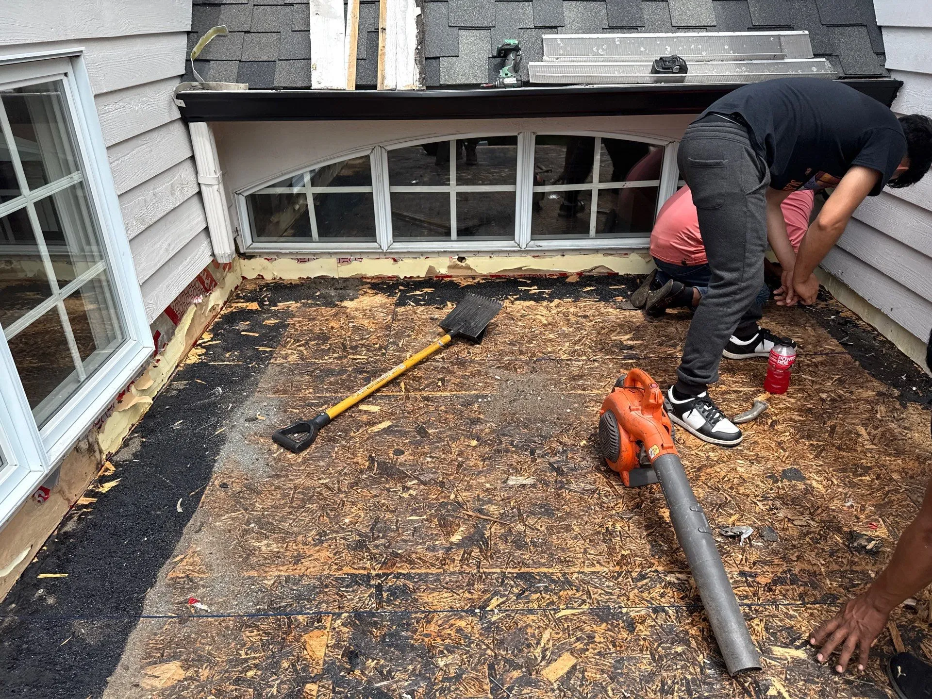 Roofer removing the old decking and cleaning between the siding and flat roof section.