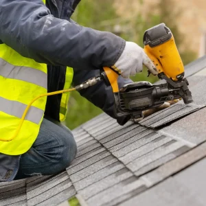 Roofer nailing shingles on with a nail gun.