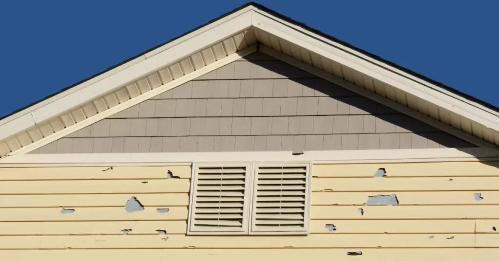 Hail damage on the side of a home with yellow vinyl siding.